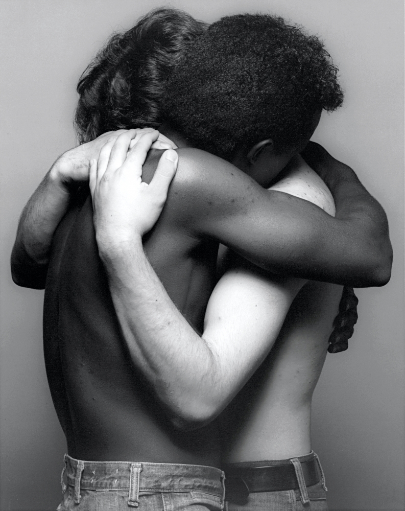Two men, one white, one Black, embracing with faces obscured.