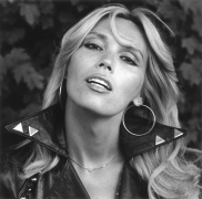 Portrait of Amanda Lear, mouth open, wearing hoops and leather jacket.