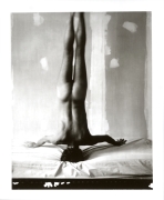 Naked man facing away from the camera doing a headstand on a bed.