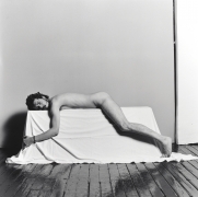 Nude white male laying prone on a white cloth box.