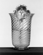 Ridged glass vase resting on a black tabletop with the top of a tulip hanging over the center edge to show the flower's interior.