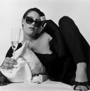 Portrait of white woman on bed holding champagne.