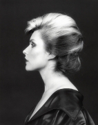 Profile view of head and shoulders of musician Debbie Harry with short blonde hair smoothly coiffed and a black silk robe opened and hanging down from her shoulders.