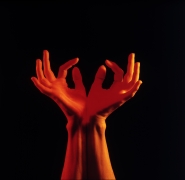 Woman's hands and wrists reaching up against a black background.