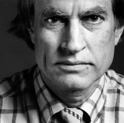 Closeup of a man with a serious expression looking into the camera and wearing a checked shirt.