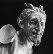 The head and shoulders of a marble statue of a devil with a beard and horns grimacing.