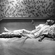 Holly Solomon in profile, reclining on bed, with a cigarette in hand.