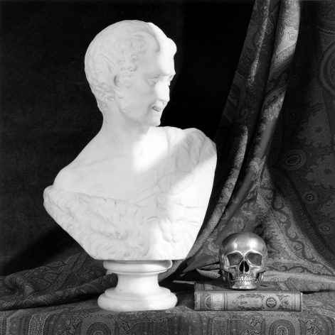 Bust of head and neck, a book, and a skull atop paisley textile.