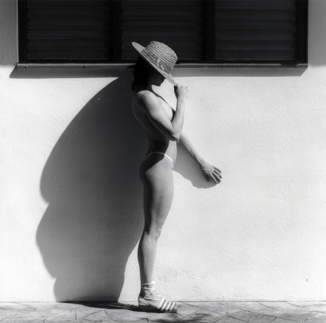 Lisa Lyon in profile, holding sun hat over her face.