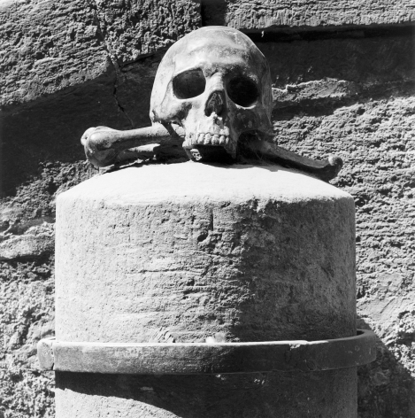 Skull and crossbones on a large stone plinth in front of a rough stone wall.