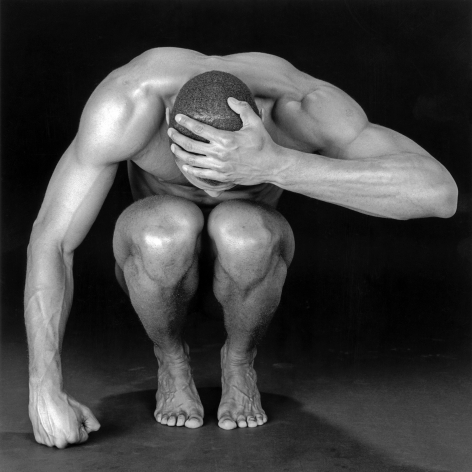 Thomas, nude, crouching with one hand on hand.