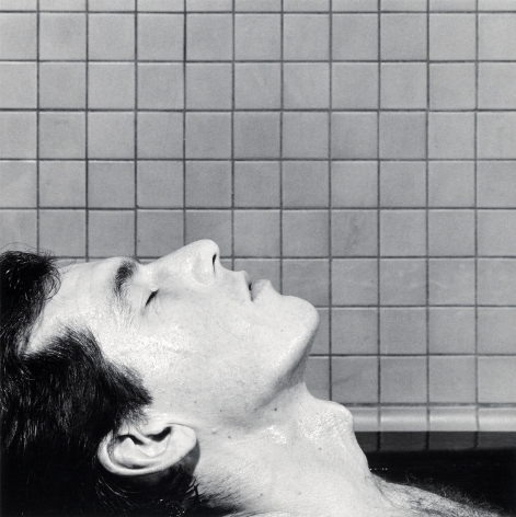 Close-up of a man in profile closing his eyes and leaning his head backward in front of a tile wall.