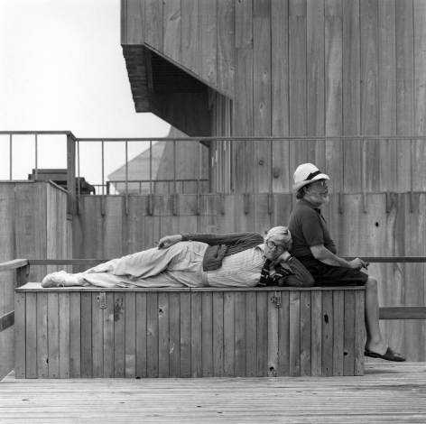 David Hockney laying on wooden bench with Henry Geldzahler sitting in profile.