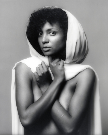 Nude woman from the waist up holding a white piece of fabric around her like a hooded cape.