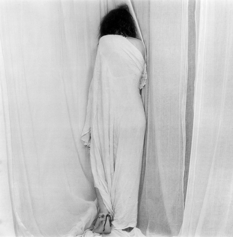 Patti Smith, wrapped in a sheet, facing corner of wall.
