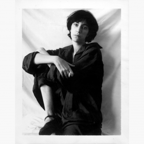 Polaroid image of Patti Smith sitting on a stool with arms wrapped around one knee.