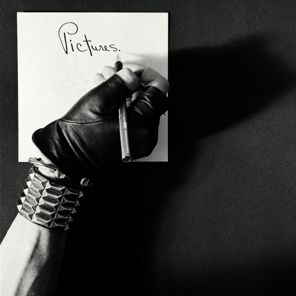 Robert Mapplethorpe's hand in leather glove and spiked bracelet writing the word "Pictures"