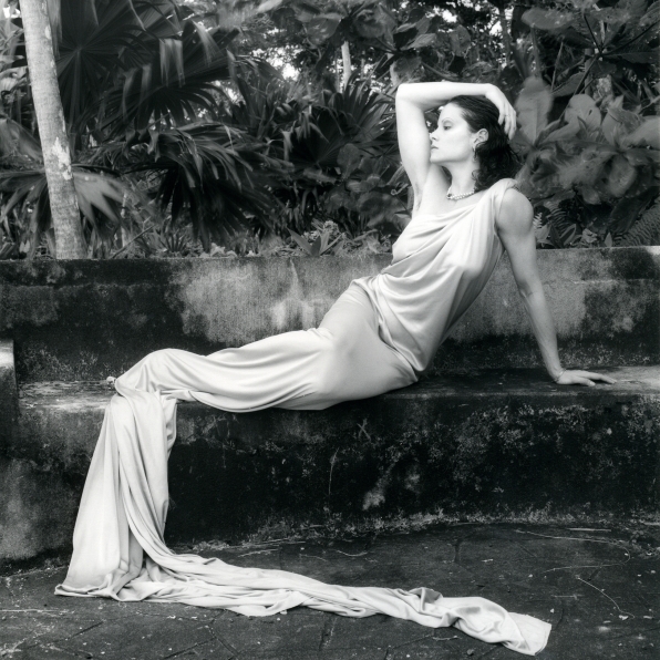  Lisa Lyon reclining in long dress, in a tropical setting.