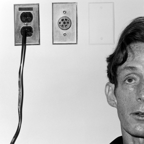 Portrait of John McKendry leaning against a wall, with electrical outlets to the left of the frame.