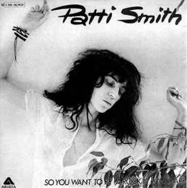 Cover of Patti Smith's album So You Want to be a Rock N Roll Star, Patti in white dress with arms raised above head looking towards lower right corner of image.