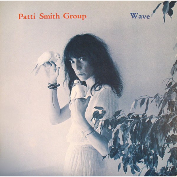 Cover of Patti Smith's album Wave, Patti leaning against a wall with a white bird in each hand, and a ficus tree in lower right corner of image.