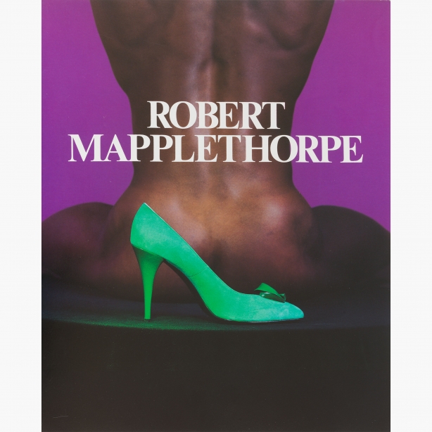 Color image of a bright green high-heeled shoe in front of a naked black man, seated and facing away from camera, against a purple background.